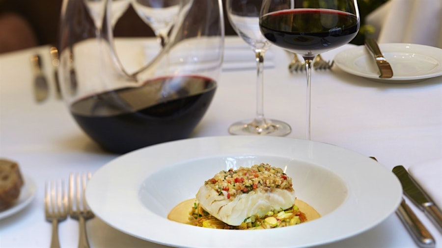 A dish of cod next to a decanter of red wine and a glass of red wine at Spruce in San Francisco